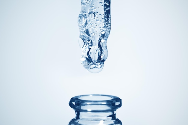 Transparent gel flowing from an eyedropper on a background with blue shades over the bottle