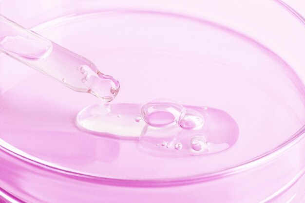 Transparent gel flowing from a pipette into a Petri dish On a pink background Closeup