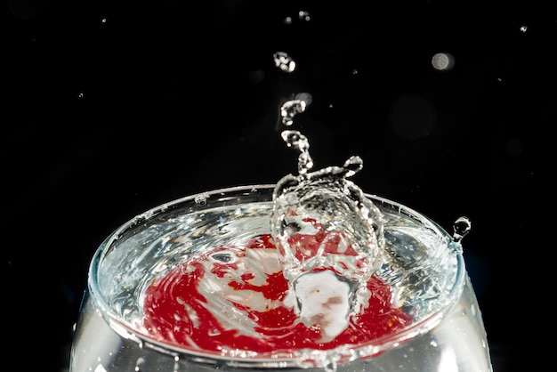 Foto ciotola di vetro trasparente riempita di acqua con riflesso rosso e gocce spruzzate effetto splash