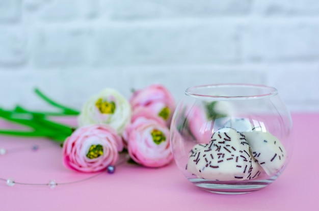 Transparent glass jar with cookies in heart shape and flowers on pink background. 