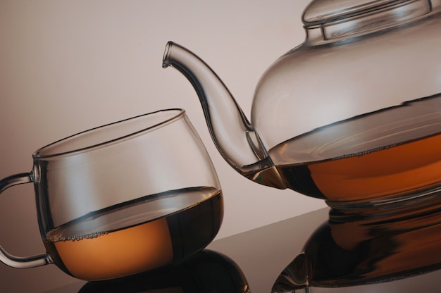 Transparent glass teapot and tea cup with reflection