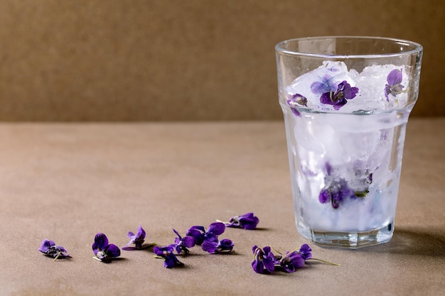 Transparent glass of violets flower crushed ice for making cold summer refreshment drink lemonade soda cocktail Standing on brown table Copy space