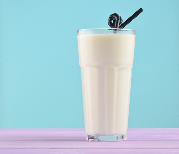 Transparent glass with fresh organic milk,cocktail tubules on a pastel color wooden table isolated on blue. Copy space