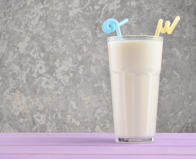 Transparent glass with fresh organic milk,cocktail tubules on a pastel color wooden table