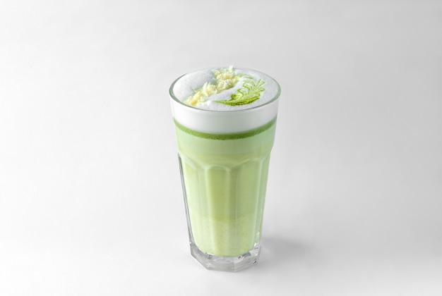 Transparent glass with green coffee latte, frothed milk, syrup, whipped cream and topping isolated on a white and gray surface