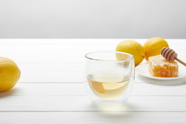 Transparent glass with green tea lemons and honeycomb on white wooden table