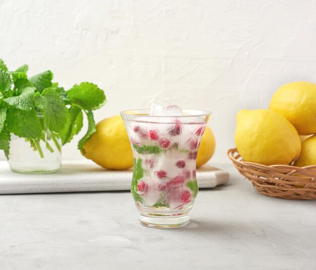 Transparent glass with lemonade and pieces of ice red berries on a white background a refres