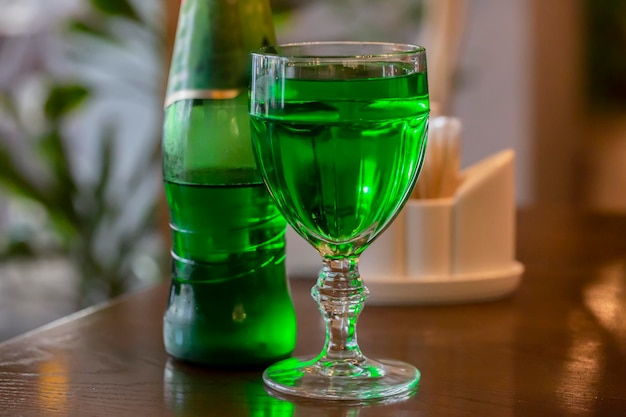 Transparent glass with a wine drink on a wooden table. Bright green drink in a glass