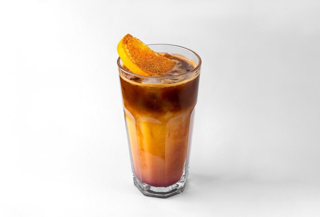 Transparent glass of yellow refreshing summer drink with sliced orange, ice cubes and chocolate syrup isolated on a white and gray background with natural shadow and copy space