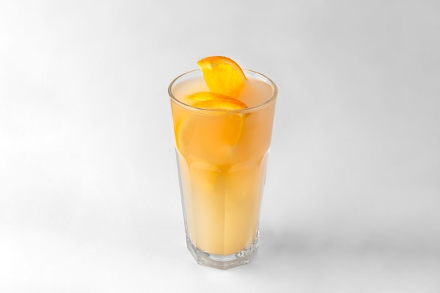 Transparent glass of yellow refreshing summer drink with sliced orange isolated on a white and gray surface with natural shadow and copy space