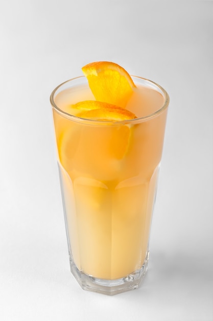 Transparent glass of yellow refreshing summer drink with sliced orange isolated on a white and gray surface with natural shadow, vertical photo