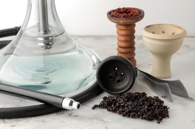 Transparent hookah with a black mouthpiece and a clay bowl with tobacco and various accessories for making hookah on a light background hookah accessories