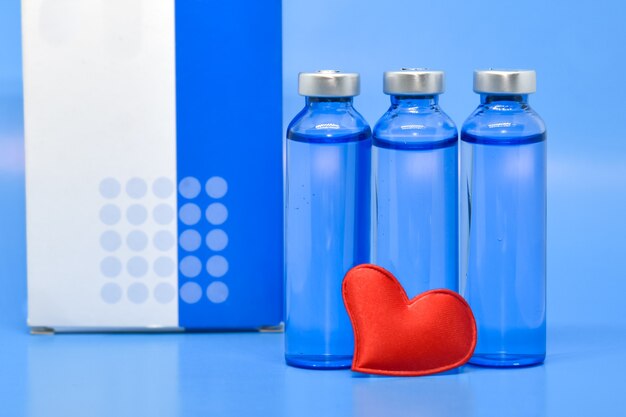 Transparent medical ampoules and red heart on light blue background. Concept: medicine, vaccination