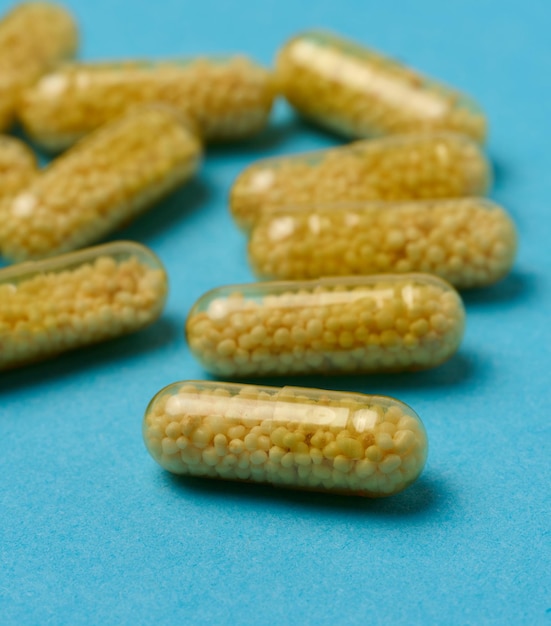 Transparent medical capsules with yellow granules inside on a blue background tablets for treatment vitamins