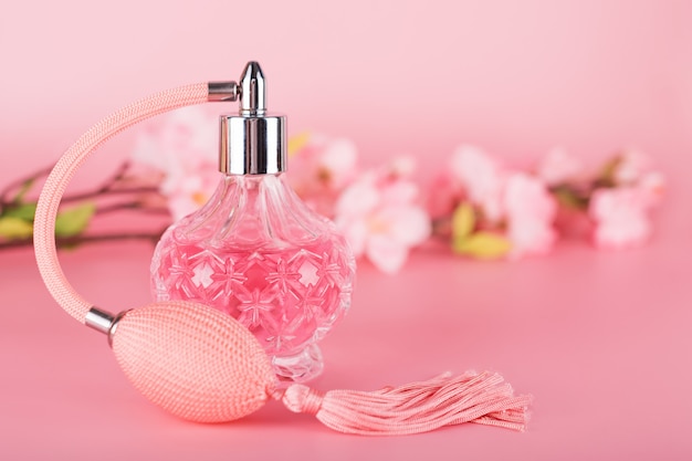 Transparent perfume bottle with spring blooming tree branch on pink background