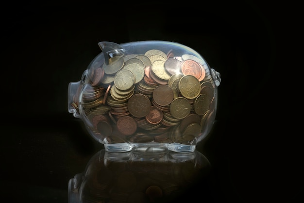 Transparent piggy bank full of euro coins on black background - savings concept - selective focus.