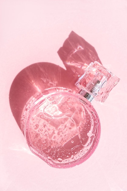 Transparent pink perfume bottle on pink background with strong shadow, top view