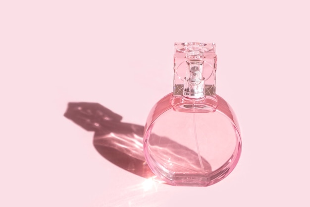 Прозрачный розовый флакон духов на розовом фоне с сильной тенью