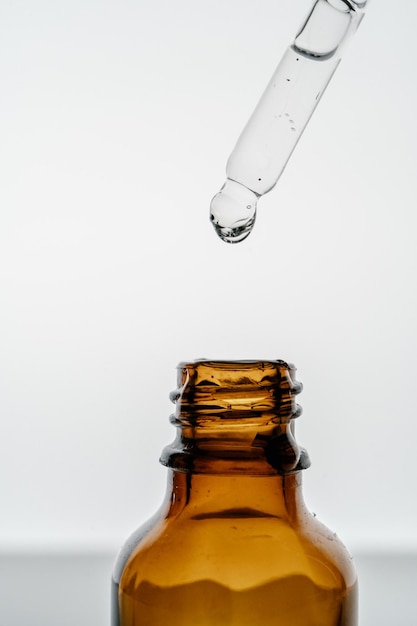 Прозрачная пипетка с косметикой и бутылкой на светлом фоне
