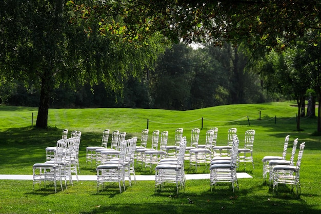 Прозрачные пластиковые стулья на свадебной церемонии на красивой зеленой лужайке