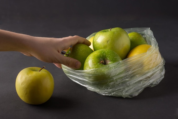 黒の背景に熟した緑と黄色のリンゴのグループと透明なプラスチック製のしわくちゃのセロハンバッグエコロジーコンセプト