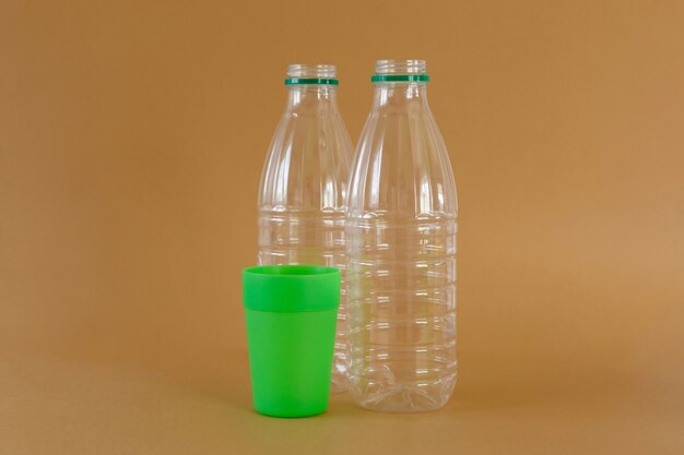 Transparent plastic milk bottles and green glass on light brown background