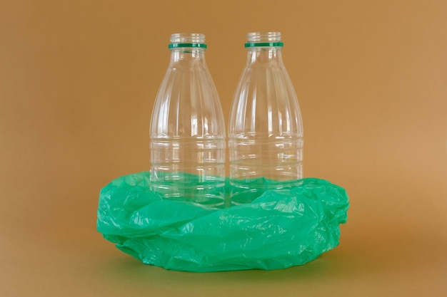 Transparent plastic milk bottles in green plastic bag on light brown background