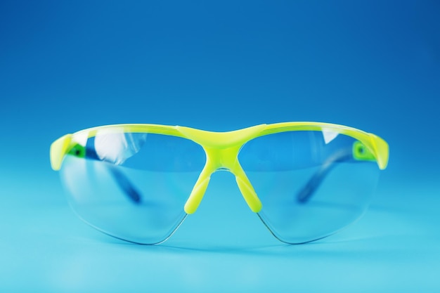 Transparent polycarbonate safety glasses on a blue background. Reliable eye protection, free space