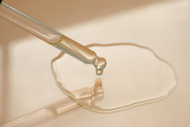 Transparent round drop of hyaluronic acid serum or oil from a glass pipette on a beige background