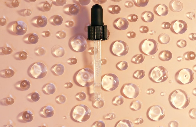 Transparent round drops of hyaluronic acid serum or oil from a glass pipette on a beige background