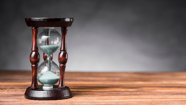 Photo transparent sand hourglass on wooden desk against gray background