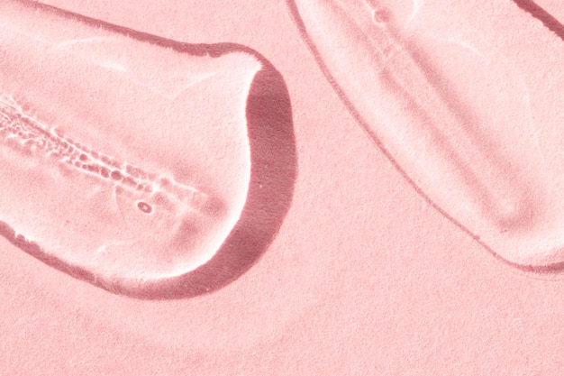 Transparent smears of liquid product gel peptide on a pink background flat lay macro