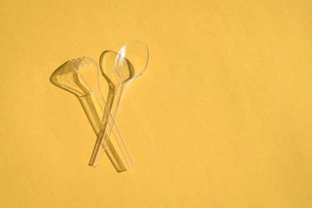 Transparent spoon and fork cutlery with shadows on yellow background