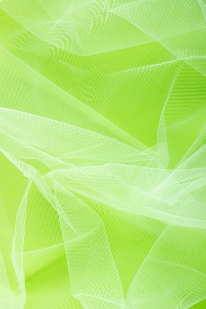 Transparent tulle fabric arranged in soft folds on a green background selective focus