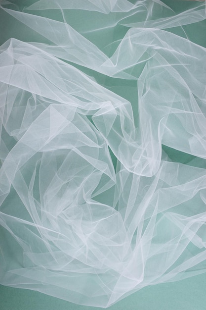 Transparent tulle fabric arranged in soft folds on a green background selective focus