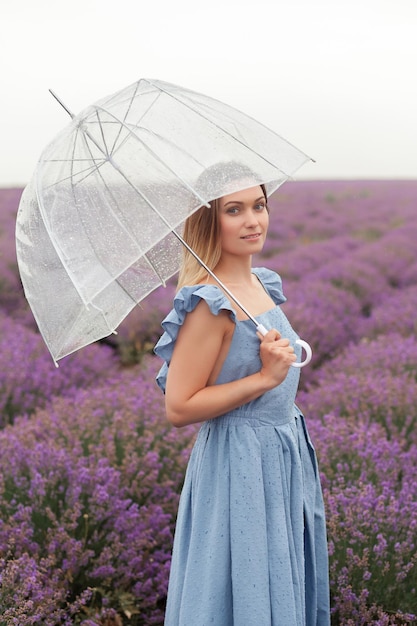 투명한 우산. 라벤더 밭에서 빗속에서 춤추는 여자. 파란색 젖은 드레스