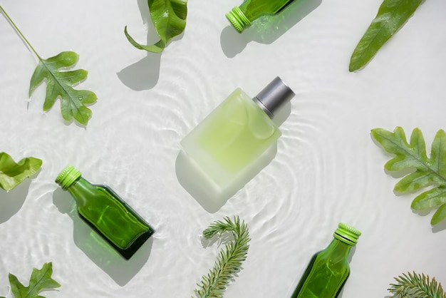 Photo transparent vial with liquid product drk glass bottles cosmetic skincare moisturizer water background splashes rings and bubbles moist green exotic leaves natural sunlight shadows