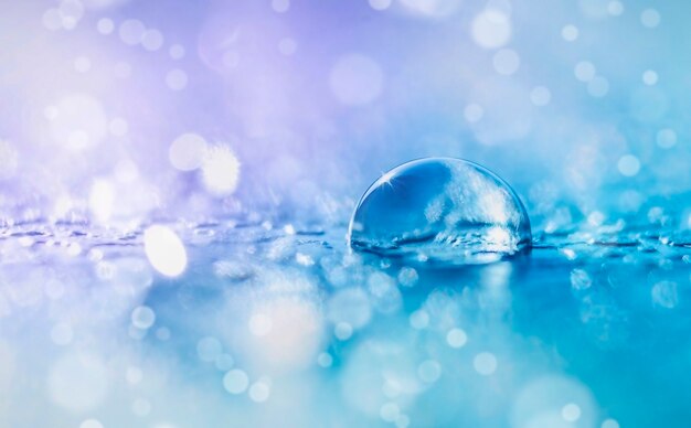 Transparent water drop on defocused background in violet and blue tones with bokeh and copy space