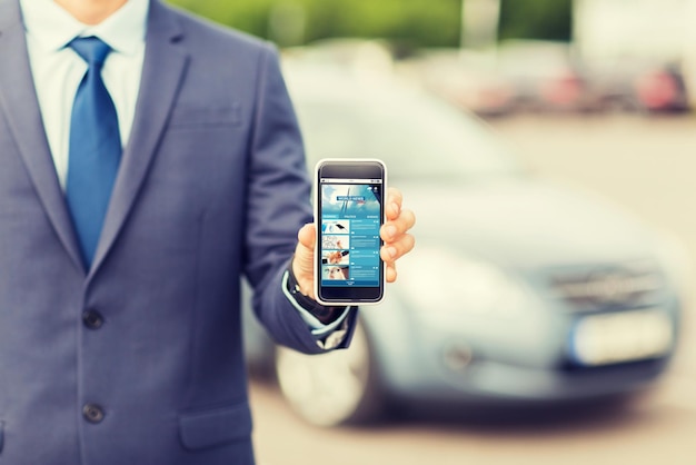 輸送、出張、マスメディア、テクノロジー、人のコンセプト – 駐車場でインターネットニュースページのスマートフォン画面を見せる男性の接写