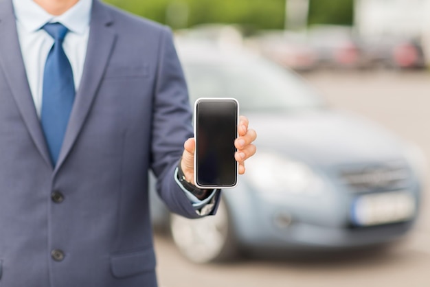 transport, business trip, technology and people concept - close up of man showing smartphone blank screen on car parking