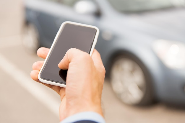 transport, business trip, technology and people concept - close up of young man hand with smartphone on car parking