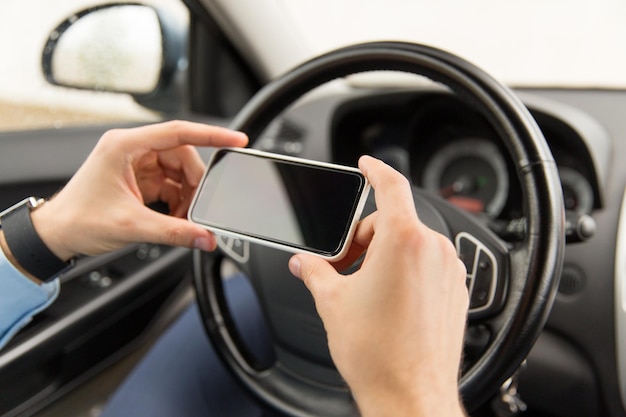 transport, business trip, technology and people concept - close up of young man hand with smartphone driving car