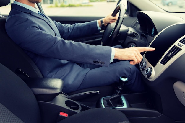 transport, business trip, technology and people concept - close up of young man in suit driving car and pointing finger to blank black computer screen on dashboard