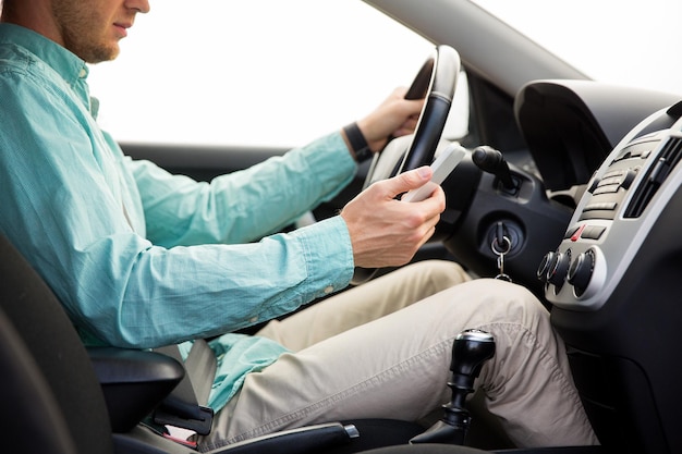 transport, business trip, technology and people concept - close up of young man with smartphone driving car