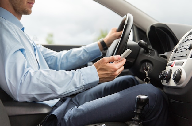 transport, business trip, technology and people concept - close up of young man with smartphone driving car