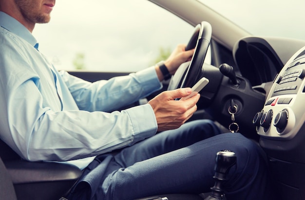 Foto concetto di trasporto, viaggio d'affari, tecnologia e persone - primo piano di un giovane con lo smartphone che guida l'auto