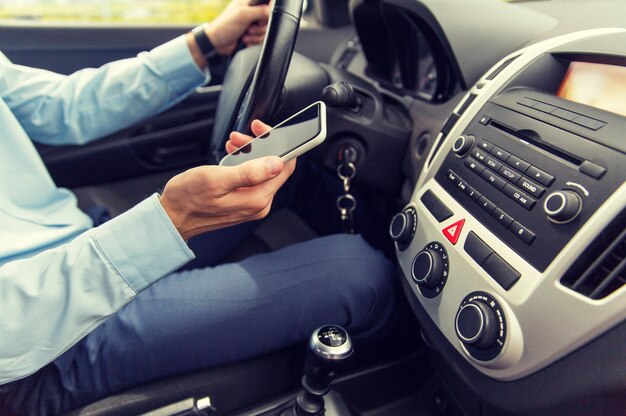 transport, business trip, technology and people concept - close up of young man with smartphone driving car