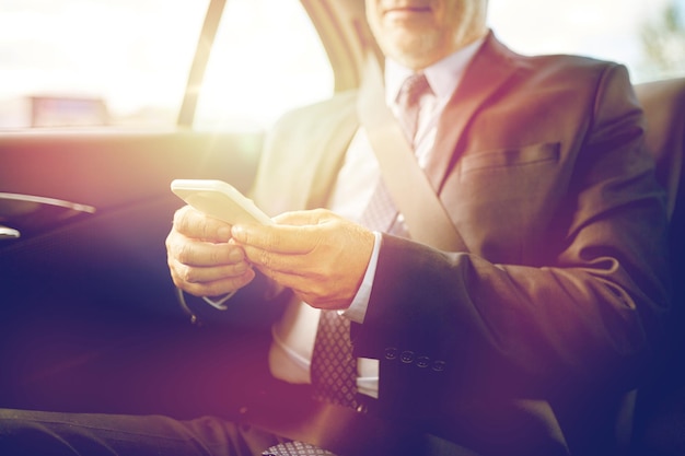 transport, business trip, technology and people concept - senior businessman texting on smartphone and driving on car back seat