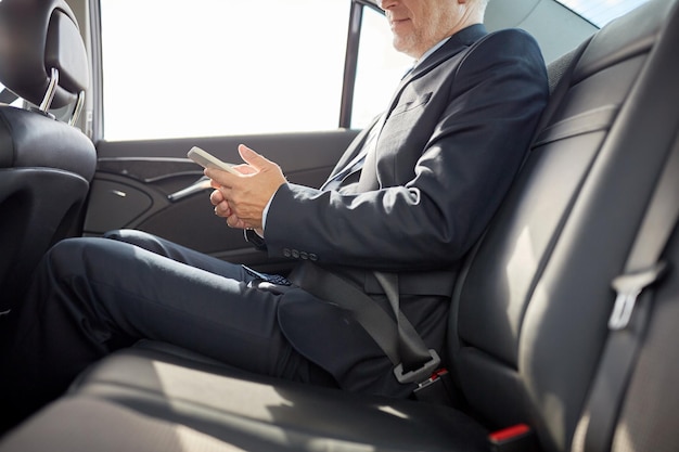 Photo transport, business trip, technology and people concept - senior businessman texting on smartphone and driving on car back seat