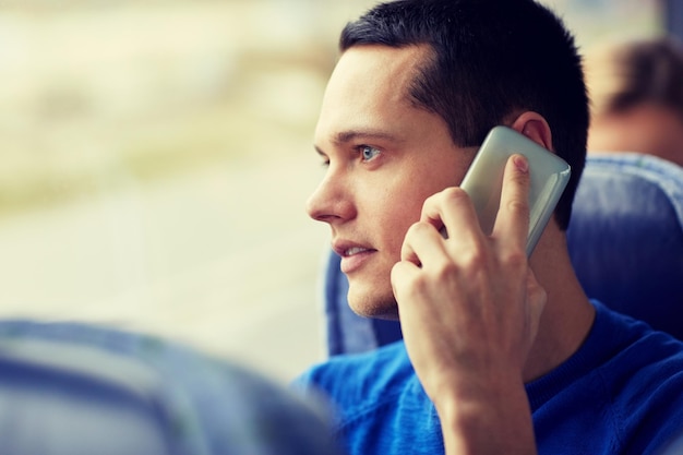 transport, toerisme, roadtrip en mensenconcept - gelukkige jonge man zit in reisbus of trein en belt op smartphone